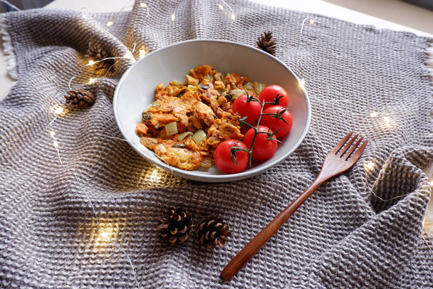 おいしいビーガンスクランブルエッグ新鮮なトマト松のコーンと小さなクリスマスライトに囲まれて - 写真・画像