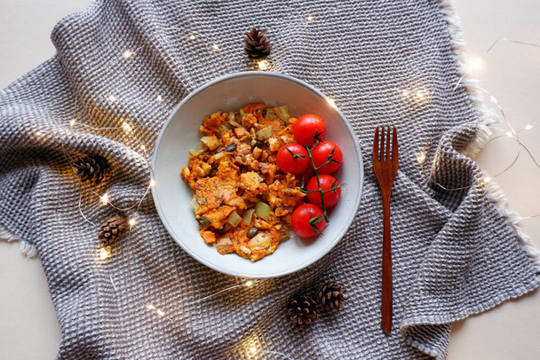 おいしいビーガンスクランブルエッグ新鮮なトマト松のコーンと小さなクリスマスライトに囲まれて - 写真・画像