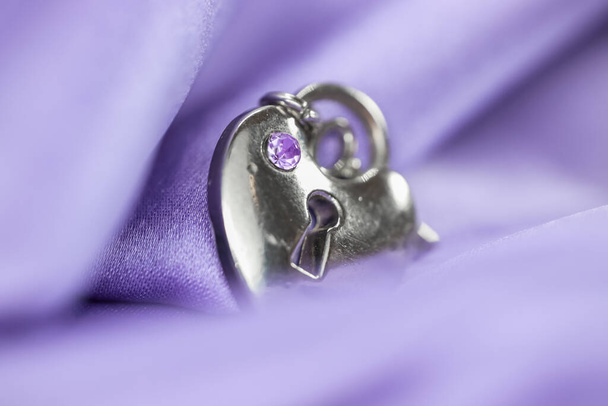 Close up shot van zilveren hanger verpakt in violette satijnen stof - Foto, afbeelding