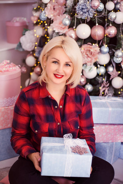 Une jeune belle fille dans une chemise rouge-noir sur le fond d'un arbre de Noël avec un cadeau dans ses mains sur une séance photo du Nouvel An dans le studio. Le concept du Nouvel An. - Photo, image