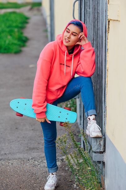 Stylish young woman with short colored hair holding blue plastic skateboard in hand. Youth concept. - Photo, image