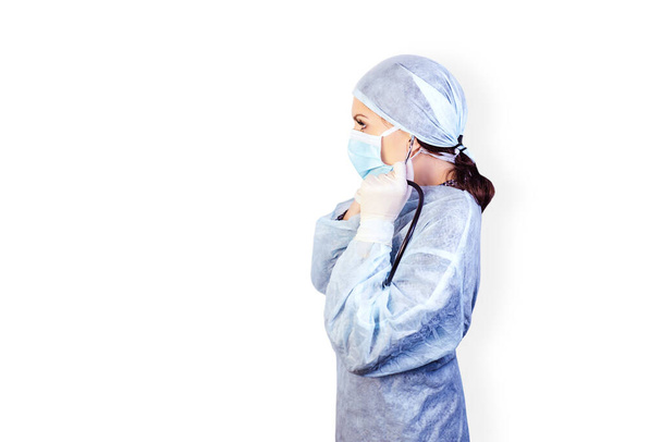 Profile portrait of a young woman doctor in medical uniform in a mask and rubber sterile gloves on a white isolated background. Coronavirus pandemic. Stay at home. - Foto, imagen