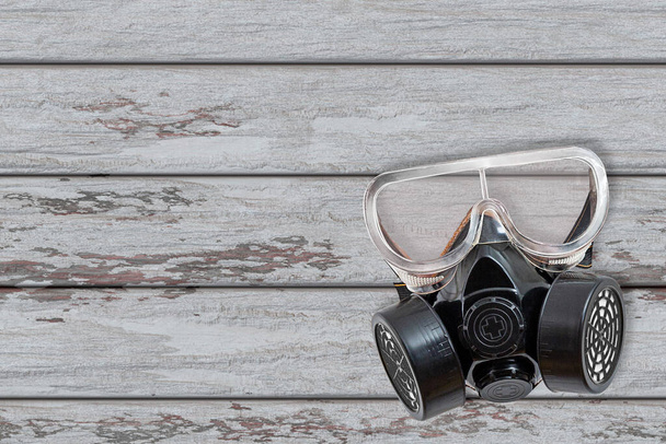 Used Respirator with filters. A black and white respirator is hanging on a wooden background. Personal protective equipment. Selective focus. Shooting outdoors. Close-up. - Photo, Image