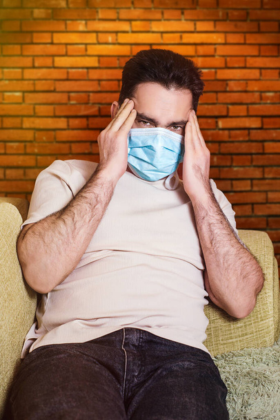 Jovem doente barbudo europeu espirra em guardanapo em casa no sofá verde. Doença, proteção, coronavírus, vírus, doença, gripe, curativo respiratório. Dor de cabeça. Calor. - Foto, Imagem