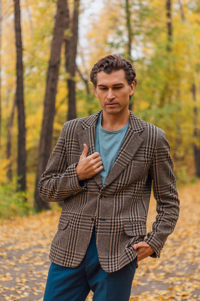 Tall handsome man dressed in a brown jacket walking on the autumn alley - Foto, Bild