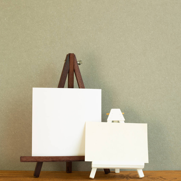 Caballete con lienzo en blanco sobre escritorio de madera. Fondo verde caqui - Foto, Imagen
