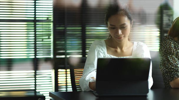 会議室でノートパソコンを操作する女性オフィスワーカーのガラス壁を通して見る - 写真・画像