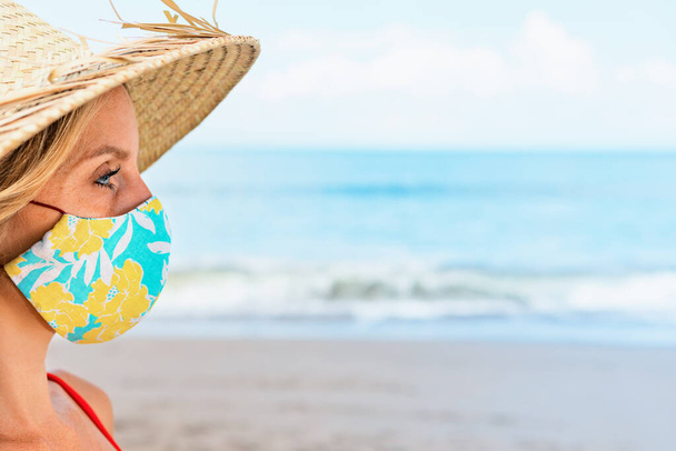 Funny portrait of young woman in straw hat on tropical sea beach. New rules to wear cloth face covering mask at public places due coronavirus COVID 19. Family holiday with kids, travel at summer 2020. - Photo, Image