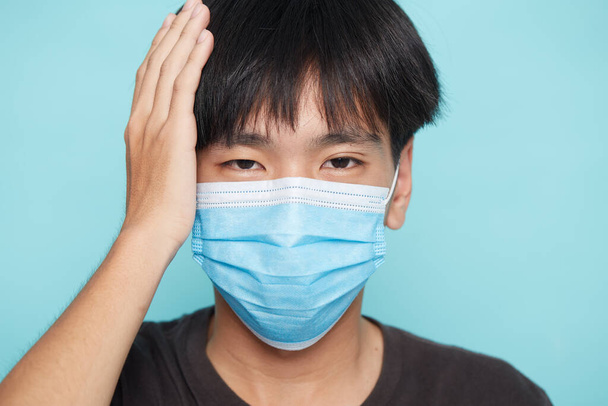 Nahaufnahme eines jungen asiatischen Mannes mit Gesichtsmaske gegen die Covid-19 auf blauem, isoliertem Hintergrund, Konzept Coronavirus - Foto, Bild