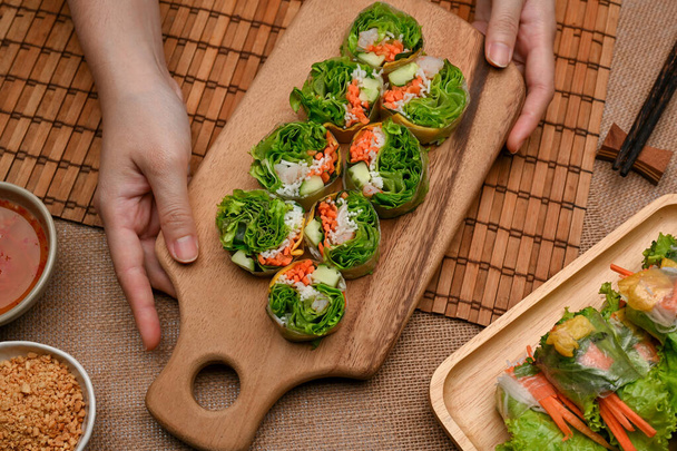 Vista superior de manos femeninas sosteniendo rollos de primavera vietnamitas en bandeja de madera, aperitivo asiático   - Foto, Imagen