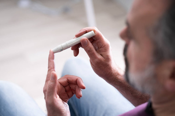 Elderly Man Using Glucometer To Check Blood Sugar Level At Home - 写真・画像