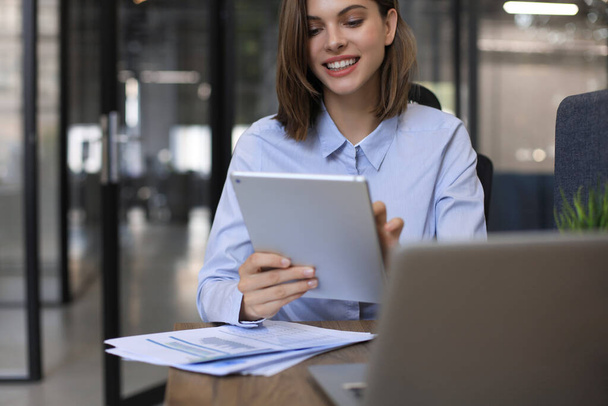 Attractive smiling woman working on a tablet in modern office - Foto, afbeelding