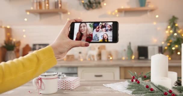 Lähikuva valkoihoinen nainen käsi tilalla älypuhelin ja video chattailuun videopuhelu verkossa ystävien ja sukulaisten ottaa useita chat uudenvuoden kotona. Joululomien juhliminen - Materiaali, video