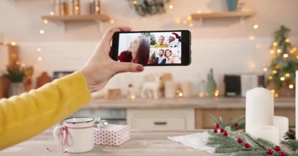 Крупный план экрана смартфона с несколькими видеозвонками в режиме онлайн с друзьями смешанных рас и родственниками европеоидами в женской руке в канун Нового года дома. Счастливого Рождества. Празднование Рождества - Кадры, видео
