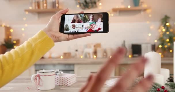 Female hand hold smartphone with multiple online video call talking with multi-ethnic Afican American friends and Caucasian relatives celebrating New Year in decorated kitchen Winter holidays Close up - Footage, Video