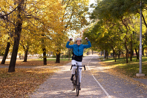 Ein junger Mann fährt mit erhobenen Händen Fahrrad im Park. Sportler in Helm und Anzug. - Foto, Bild