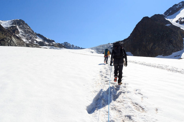 氷河の上のクランポンとロープチームの登山タシャフナーとチロルアルプス、オーストリアの青い空と山の雪のパノラマ - 写真・画像