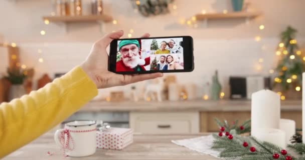 Close up of cellphone with online conference video with mixed-races people. Videochatting with African American friends and Caucasian old man in Santa costume on Christmas. Multiple video chat concept - Footage, Video