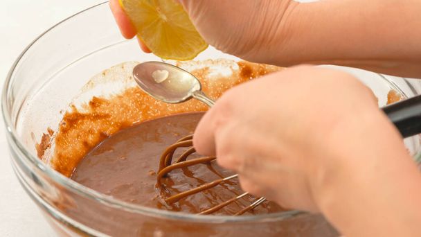 Рецепт шоколадных кексов. Женщина втискивает лимонный сок в миску, закрывает обзор, светлый фон - Фото, изображение