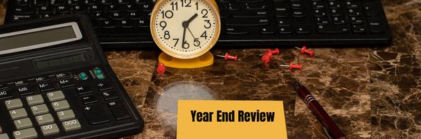 YEAR END OVERVIEW, geschrieben auf einem Blatt Papier, das auf einem Marmortisch neben einer gelben Uhr, einem Stift und einem Taschenrechner liegt. Finanzbericht zum Jahresende. Geschäftskonzept - Foto, Bild