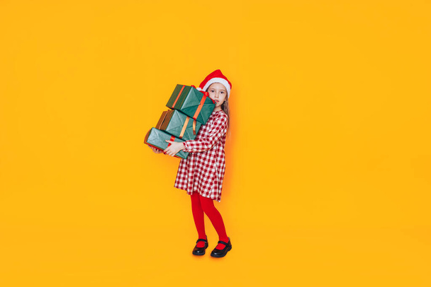 Child holding a box in green packaging with a gift. Christmas mood. She has a santa hat on her head. - Fotó, kép