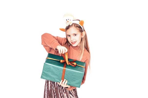 Child holding a box in green packaging with a gift. Christmas mood. She has antlers on her head. - Photo, Image