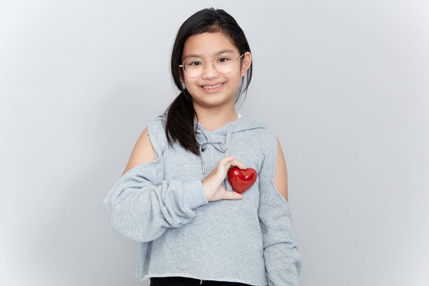 Πορτρέτο ενός μικρού κοριτσιού που κρατά μια κόκκινη καρδιά Σχήμα σε γκρι φόντο - Φωτογραφία, εικόνα