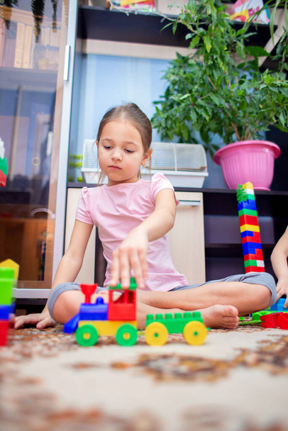 Ein kleines Mädchen sitzt zu Hause auf dem Fußboden und spielt einen bunten Plastikbauer. Ein Kind spielt mit einer Spielzeugeisenbahn - Foto, Bild