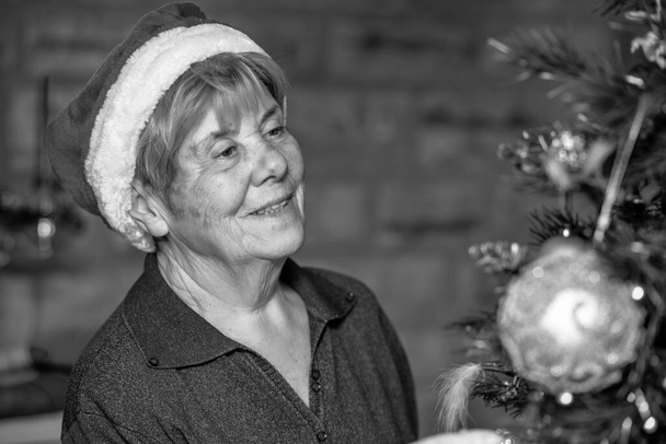 Noel ağacını süsleyen kırmızı şapkalı mutlu, emekli kadın.. - Fotoğraf, Görsel