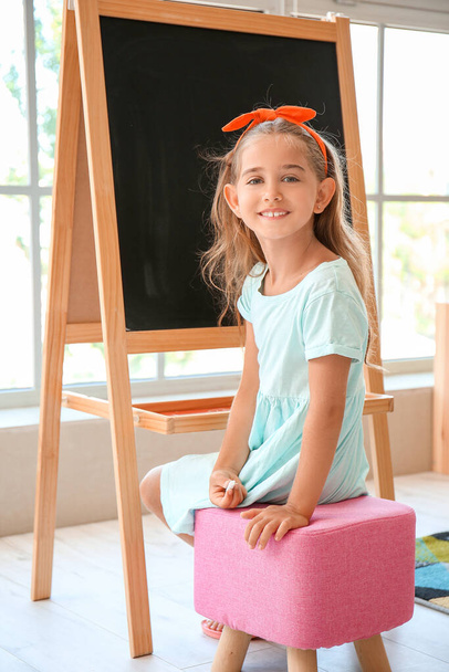 Glückliches kleines Mädchen mit Kreide neben Tafel im Kindergarten - Foto, Bild