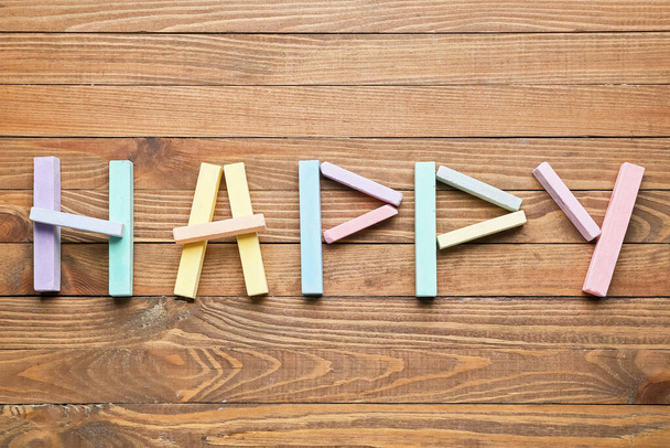 Pieces of color chalk and text HAPPY on wooden background - Zdjęcie, obraz