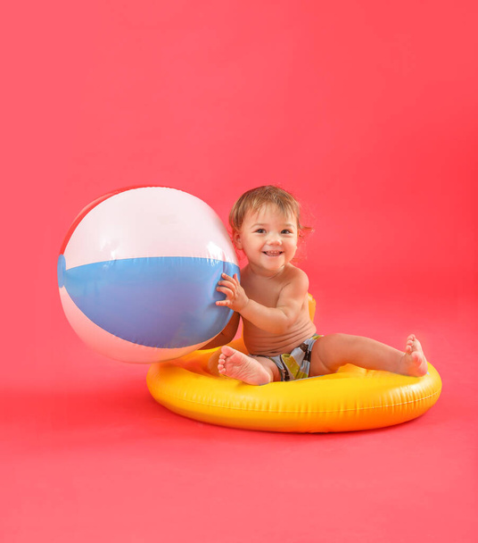 Cute baby boy with inflatable ring and beach ball on color background - 写真・画像