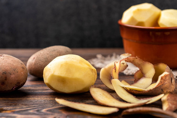 Raw peeled potatoes in bowl on dark wooden background. - Photo, Image