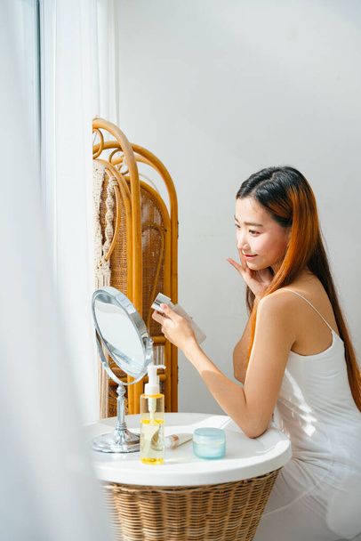 Schöne junge asiatische Frau macht Make-up vor dem Spiegel zu Hause. - Foto, Bild