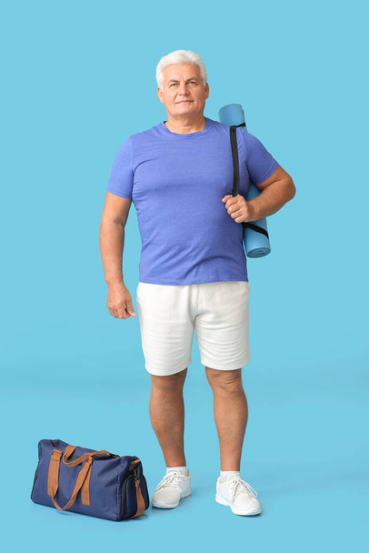 Homme âgé sportif avec sac et tapis de yoga sur fond de couleur - Photo, image