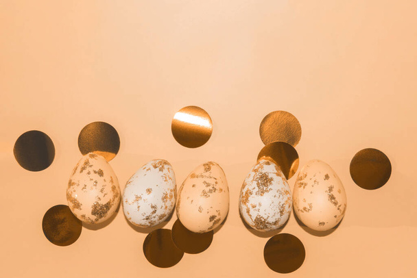 peach and white Easter eggs painted with gold with round golden confetti - Photo, Image