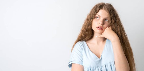 Photo of Pensive European young woman with curly long hair, looking up having pensive expression. Isolated over white background. Copy space for your text - 写真・画像
