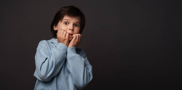 I'm afraid. Image of scared boy 10-12 years old in casual clothes covering his mouth with hands. Fright, phobia, panic attack, horror and facial expression concept. Studio shot, gray background - Photo, Image