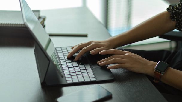 Вид збоку жіночих рук, що друкуються на клавіатурі планшета на робочому столі в офісній кімнаті
 - Фото, зображення