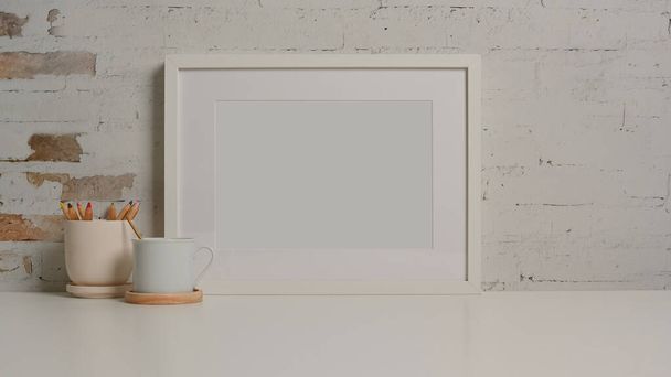 Close up view of white desk with mock up frame, papeteria, kubek i przestrzeń do kopiowania w salonie - Zdjęcie, obraz
