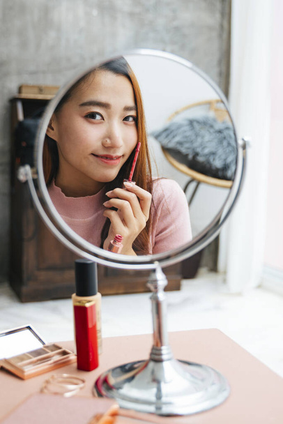 Красива азіатська жінка наносить помаду на дзеркало вдома
. - Фото, зображення