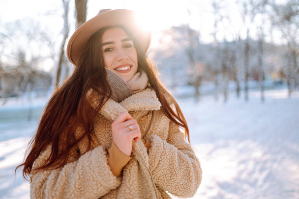 Stylish woman enjoying winter moments in a snowy park. Young woman in winter clothes posing with joy outside, frosty day. Youth, fashion, lifestyle and leisure concept. - Photo, Image
