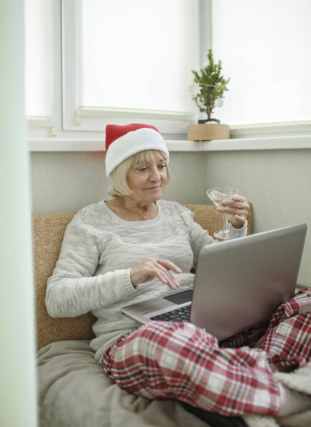 Безпечне онлайн-святкування. Старша жінка тримає келих вина і святкує Різдво зі своєю сім'єю практично через інтернет і блокнот вдома. Відеодзвінок. Віддалений відпочинок, внутрішній спосіб життя
 - Фото, зображення