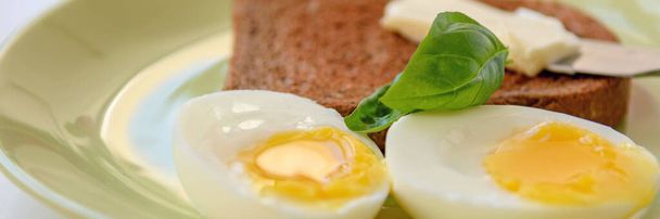 皿の上に半熟卵が2つ。バジルの葉、トーストとバター。閉じろ!. - 写真・画像