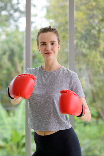 Portret van jonge fitness sportieve vrouw in sportkleding met rode bokshandschoenen ponsen hit. gezond leefstijlconcept - Foto, afbeelding