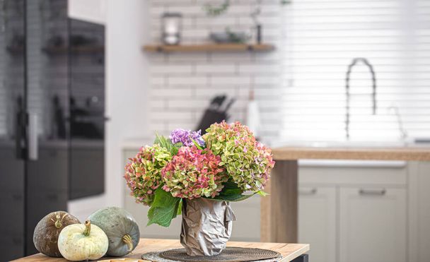 Autumn composition of colored flowers of hydrangeas and pumpkins on a blurred background of the interior of a light modern kitchen close up. - Photo, Image