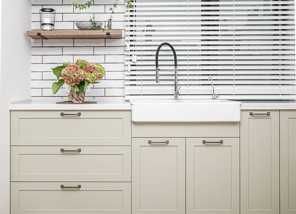 Kücheneinrichtung mit weißen Küchenschränken mit Metallgriffen und einem Blumenstrauß auf dem Tisch. - Foto, Bild