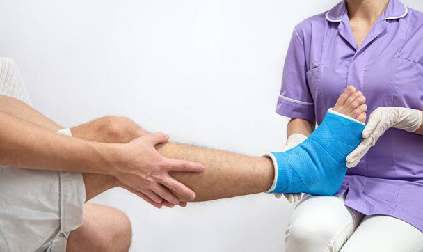 Primo piano della gamba di un uomo con un gesso e una stecca blu dopo la fasciatura in ospedale. - Foto, immagini