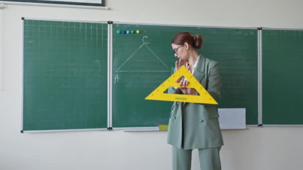 πορτρέτο του σύγχρονου δασκάλου κοιτάζοντας κάμερα και λέει, παιδαγωγική σε γυαλιά με χάρακα στα χέρια καταγράφει βίντεο μάθημα στέκεται στον πίνακα στο σχολείο - Πλάνα, βίντεο