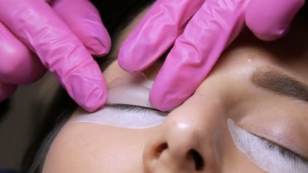 Moderna procedura di laminazione delle ciglia in un salone di bellezza professionale. Il maestro applica speciali bigodini in silicone prima della procedura di arricciatura delle ciglia - Filmati, video
